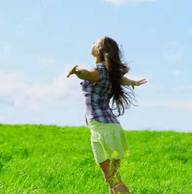 Persona alzando los brazos en un campo verde